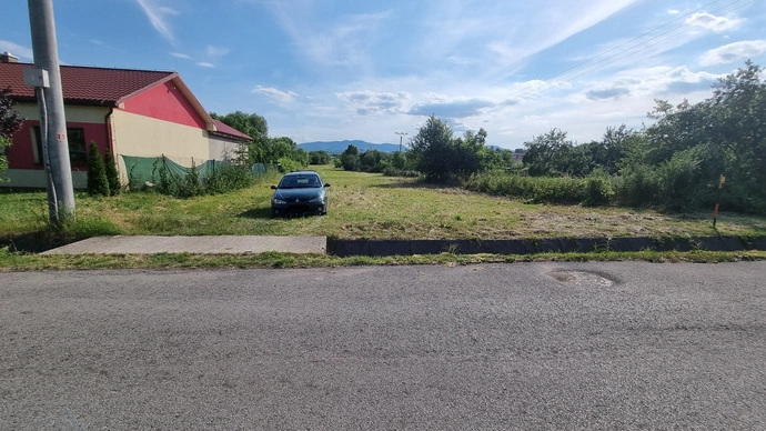 Fotografia pozemku, na ktorej dobre vidieť dostupnosť sietí: Na ľavo stĺp elektrického vedenia, z ktorého je možné ťahať elektrickú prípojku, smerom na pravo na ceste kanalizačná šachta predstavuje existenciu kanalizácie a ešte orandžovo čierna tyč znázorňujúca plynové potrubie.